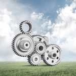 Abstract mechanism with cogwheels on green meadow