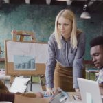 Blonde woman team leader giving direction to mixed race team of young guys. Creative business meeting at modern office.